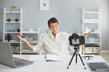 Confident female vlogger recording video on camera sitting at her desk in cozy home office