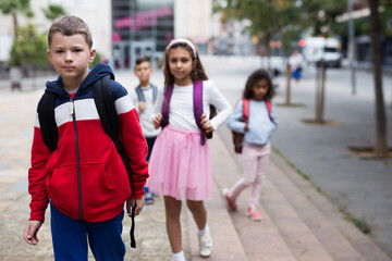 Obraz premium Portrait of positive boy standing near school, children on background