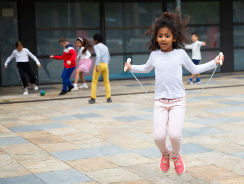 Happy schoolgirl jumping game by rubber band, kids friends on background