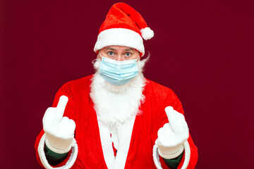 Bad Santa Claus showing the middle finger,he wears a medical mask.Red wall.