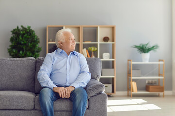 Senior man sitting on sofa in living room thinking about life and recollecting memories of the past