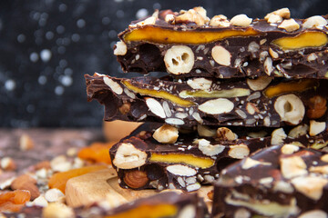 Close-up of dark chocolate pyramid with hazelnuts, mango, sesame and almonds on wooden board with dark blurred background