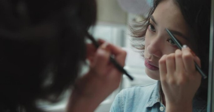 beautiful Asian woman with curly hair, in front of the bathroom mirror, carefully drawing her eyebrows and arranging her hair young lady make up in the morning 