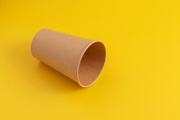 Empty cardboard coffee cup on a yellow background.