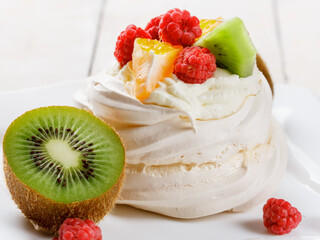 Pavlova sweet cream dessert with berries and fruits on white wooden background. Delicious food.