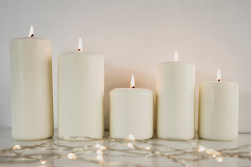Large burning candles on the background of a white wall.