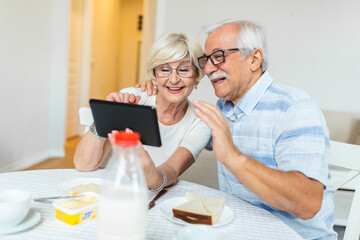 Senior couple smiling and looking at the same tablet hugged. Indoor, at home concept. Mature and retired man and woman using technology - lockdown and quarantine lifestyle