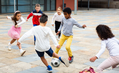 Cheerful tween schoolchildren gaily spending time together on warm spring day, playing with ball...