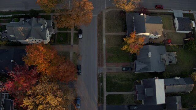 Aerial pulling back and tilting up over a beautiful street in a Kirkwood neighborhood in St. Louis, Missouri in Fall at peak color on a pretty evening at golden hour.