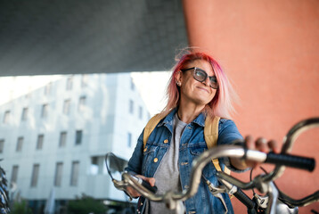 Senior woman with purple pink hair and bicycle standing outdoors in city or town. - Powered by Adobe