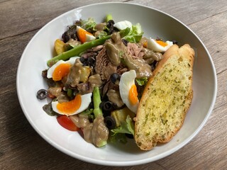 Nicoise salad with tuna, green asparagus, anchovies, fried potatoes, olives, herb and garlic bread