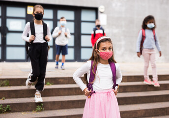 Portrait of schoolgirl in medical mask standing on the street, kids on background
