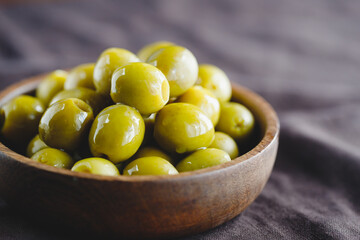 Green olives in a wooden bowl on a table, macro photography.