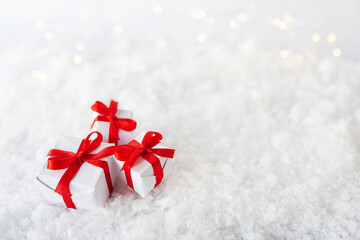 Decorative white gift boxes with red bow standing in snow against a background bokeh of twinkling party lights