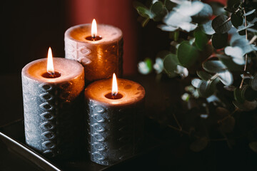 Black burning candles against dark red background with eucalyptus branch.