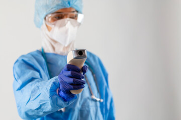 A digital thermometer device in a hand of an Asian female scientist or nurse in PPE uniform....