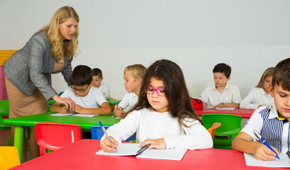 Fototapeta na wymiar Female teacher helping schoolchildren doing their task in classroom