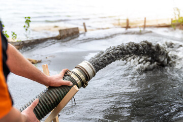 Engeneer hold pipe of power pump machine pouring mud sludge waste water with sand silt on ground....