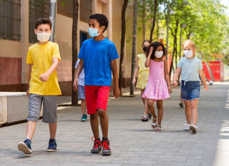 Schoolchildren in masks walking together on the street from school