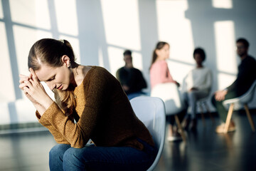 Young sad woman sitting apart from attenders of group therapy at community center.