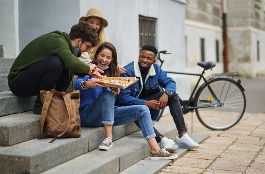 Group Of Young People Outdoors In Town, Eating Pizza. Coronavirus Concept.