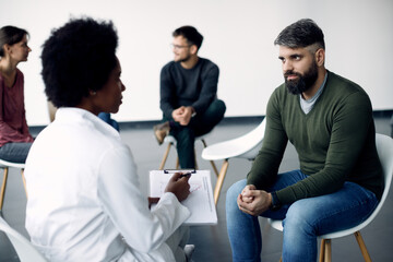 Fototapeta premium Mid adult man talking to female psychotherapist during group meeting.