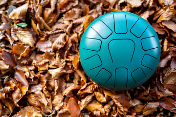Hand pan tongue drum relaxing musical instrument placed on the right of the frame against a dark brown background of dry and colorful autumn leaves. Hobbies and leisure activities. Copy space