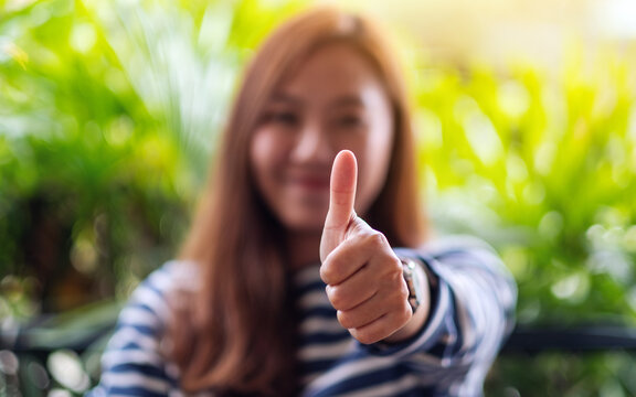 Closeup image of a young asian woman making and showing thumbs up hand sign