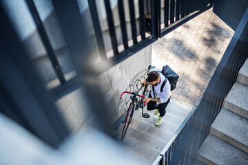 Young man commuter with bicycle walking up the stairs outdoors in city.