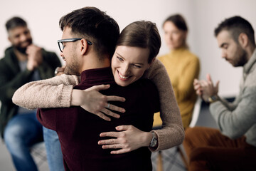 Happy woman embracing one of attenders of group therapy during the meeting.