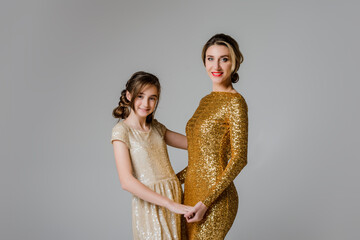 Lovely and elegant mother and daughter, in beautiful fashionable dresses with hairstyles over gray bakcground. Beauty and fashion. Mom and daughter