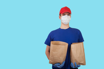 Young male volunteer in a medical mask in rubber gloves holds two packages with humanitarian aid on a blue background .. Social concept. Delivery of goods by courier. Copy spaes