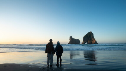 Couple standing on Wharariki Beach and watching  the Archway Island at Sunset, South Island of New...