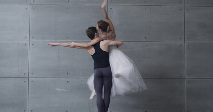 Elegant couple of classical ballet dancers dancing on a gray background, cinematic shooting of a romantic dance of ballet dancers, a young couple engaged in choreography.