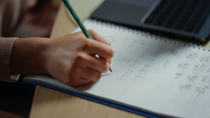 Student hand writing in notebook indoors. Unknown girl doing homework inside.