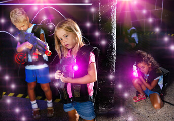 Smiling girl aiming laser gun at other players during lasertag game in dark room. High quality photo