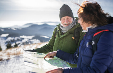 Senior couple hikers using map in snow-covered winter nature.