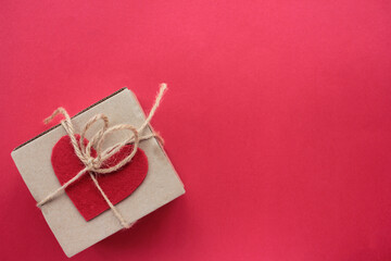 Craft gift box with tied with twine and decorated with handmade felt fabric heart on red background. Flat lay valentine`s day composition/ Copy space