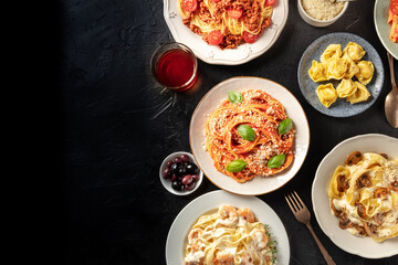 Italian food, overhead flat lay shot. Pasta, olives, wine on a black background with copy space. Spaghetti with tomato sauce, ravioli, and other classic dishes
