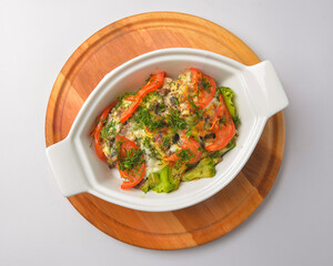 Baked mixed vegetable casserole with broccoli and tomatoes. Served in a white pot over white background.