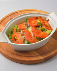 Baked mixed vegetable casserole with broccoli and tomatoes. Served in a white pot over white background.