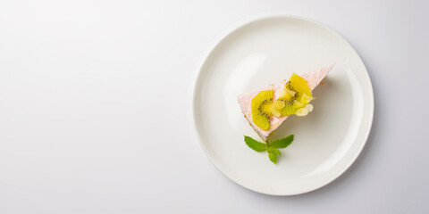 Fruit cake with kiwi and mint. One piece of fruit sweet cake dessert served on a big white plate over white background.