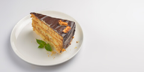 Caramel and chocolate cake with mint served on a white plate over white background.