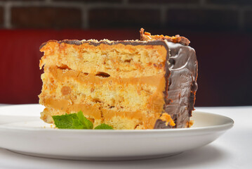 Caramel and chocolate cake with mint served on a white plate over white background.