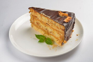 Caramel and chocolate cake with mint served on a white plate over white background.