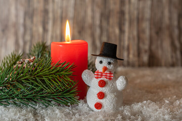 Burning red candle with a little snowman in the snow, copy space