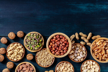 Many different nuts, shot from the top on a dark blue background with a place for text. Hazelnuts and pistachios, pine nuts and cashews, almonds and peanuts with a place for text