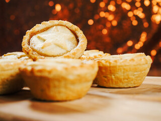 Mince pies on a wooden board and table. Glitter bokeh background. Close up. Christmas theme snack. Pastry product for special season