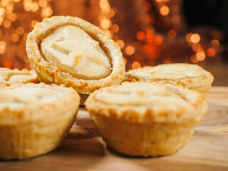 Fresh mince pies on a wooden board. Traditional Christmas pastry product. Warm glitter bokeh background