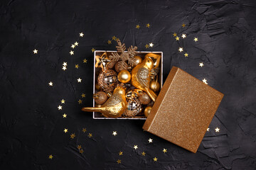 Gift box filled with golden christmas decorations on a black background.